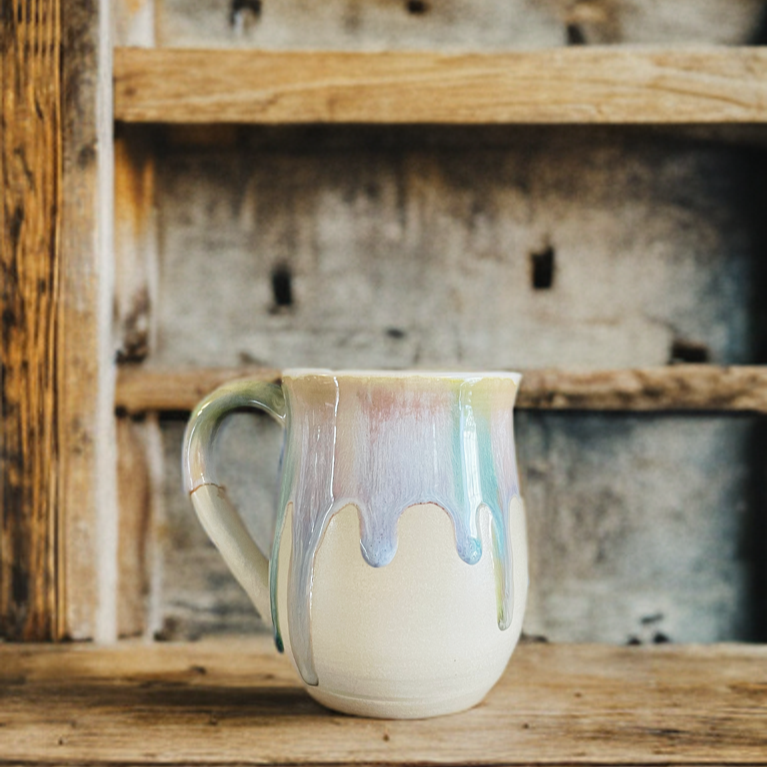 Melting pastel colours on a white clay potbellied mug on a wooden shelf with a rustic background