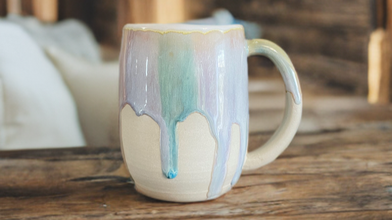 Melting pastel colours on a white clay barrel mug on a wooden shelf with a rustic background
